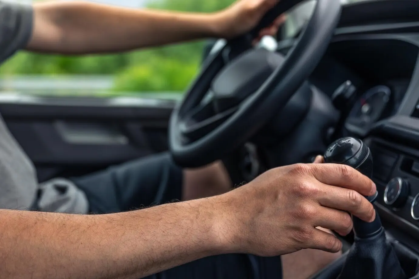 Ручное управление автомобилем: руки на руле и рычаге коробки передач, автомобиль в движении.